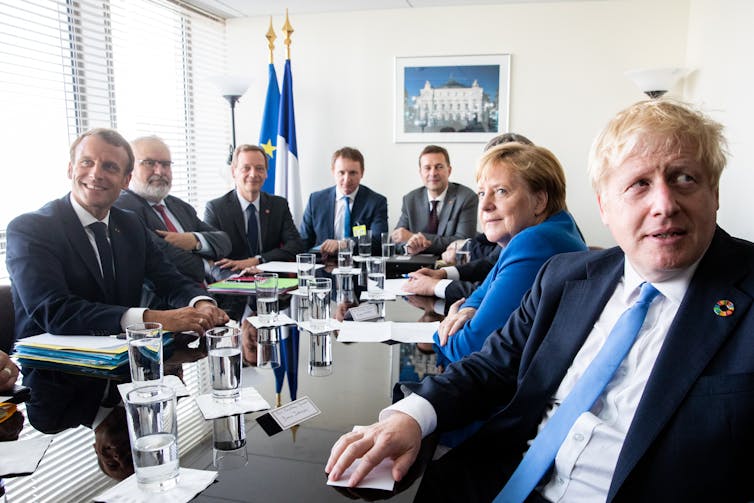 Emmanuel Macron, Angela Merkel and Boris Johnson sit at a table with diplomats.