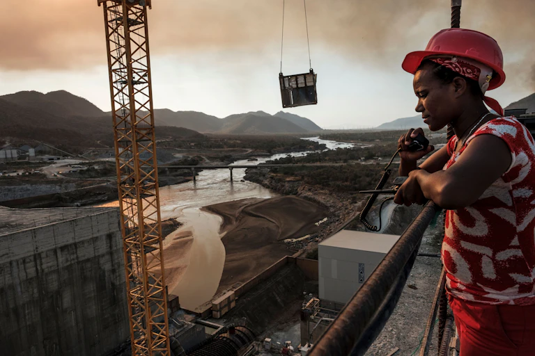 Man wearing a hard hat standing at a point overlooking dam construction site with crane