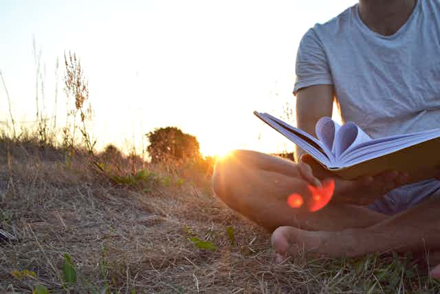 Una persona descalza leyendo ante una puesta de sol. Las hojas del libro forman un corazón.