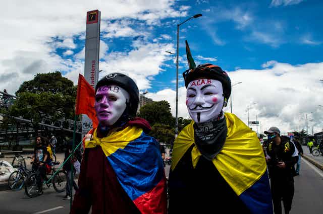 Dos manifestantes con máscaras y sendas banderas de Colombia atadas al cuello.