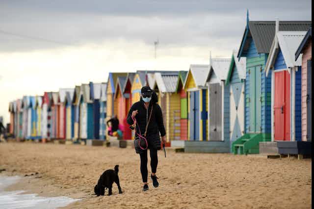 A person walking their dog on the beach wearing a mask