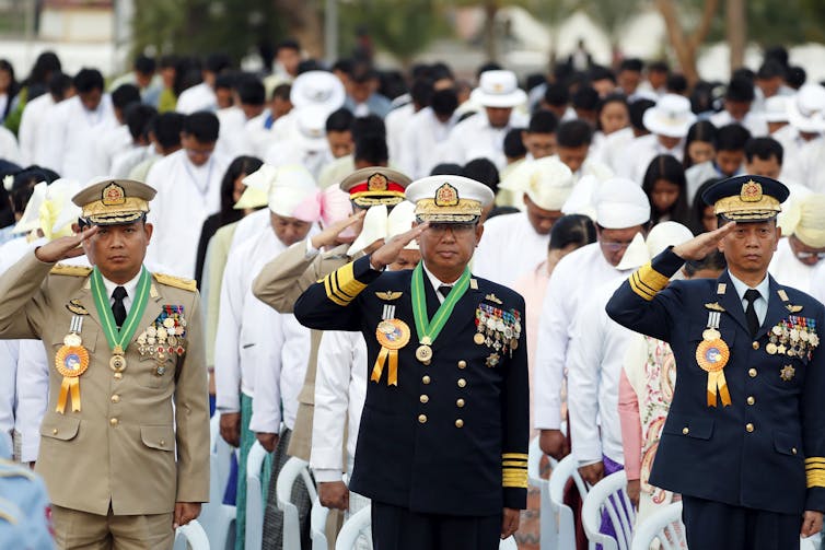 Myanmar military officers salute at their national flag during a ceremony.
