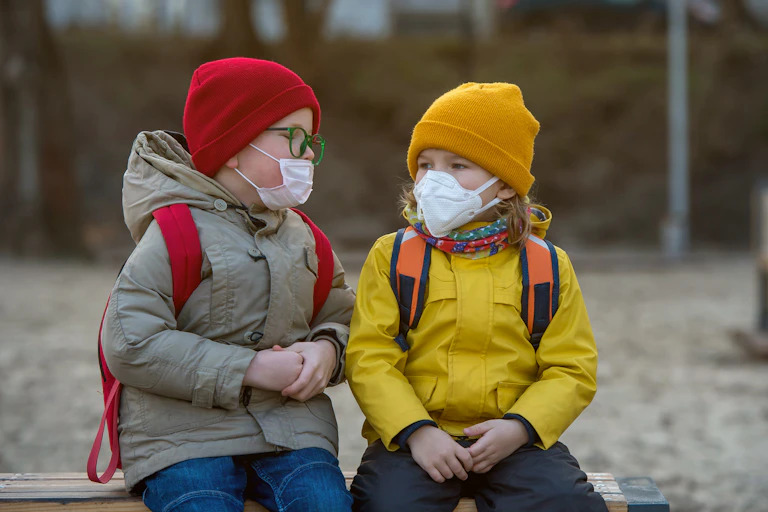 Two young children in masks on a bench.