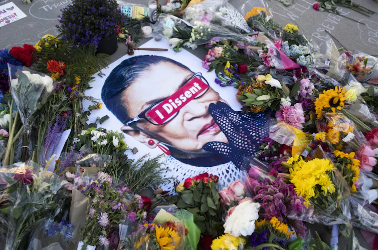 Photo of Ruth Bader Ginsburg on pavement surrounded by flowers.