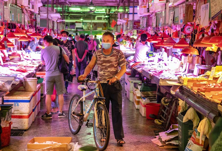 A man with a bicycle, wearing a face mask, standing in a Chinese wet market