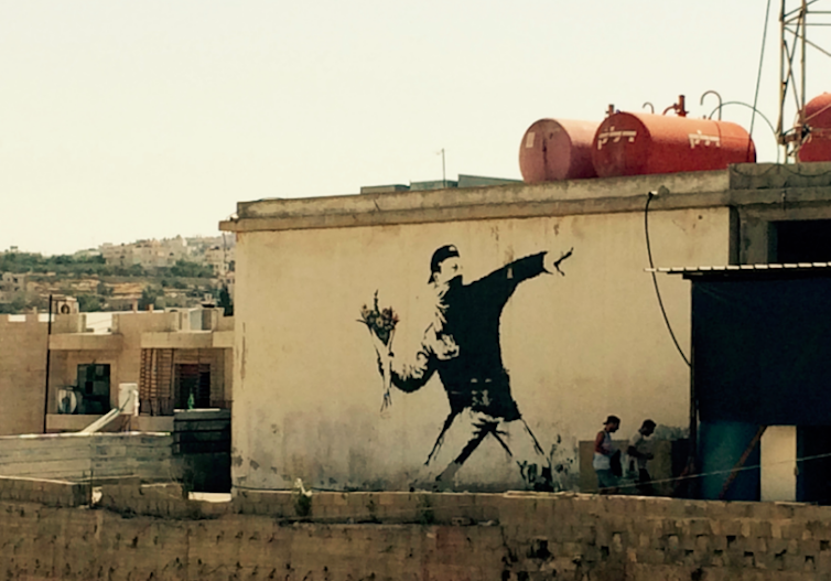 White wall showing Banksy's Flower Thrower, which shows a masked youth throwing a bunch of flowers instead of a rock or a Molotov cocktail.