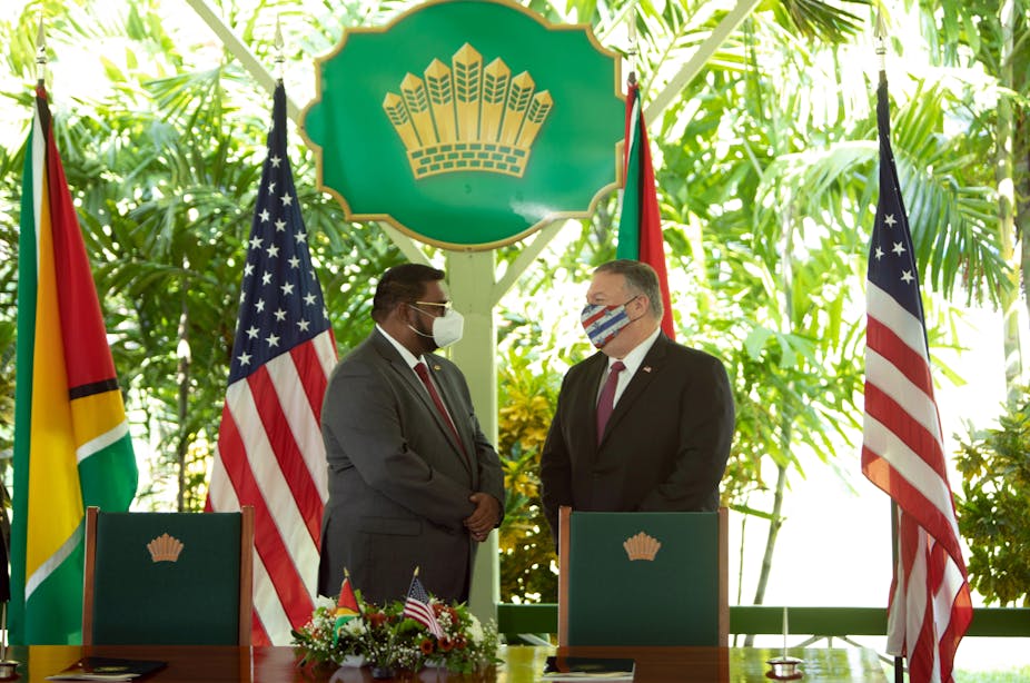 Pompeo and Ali stand in front of their respective flagswearing face masks against a verdant Caribbean backdrop