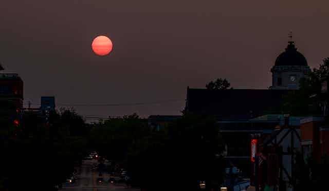 A red sun setting over a town with a clocktower. 