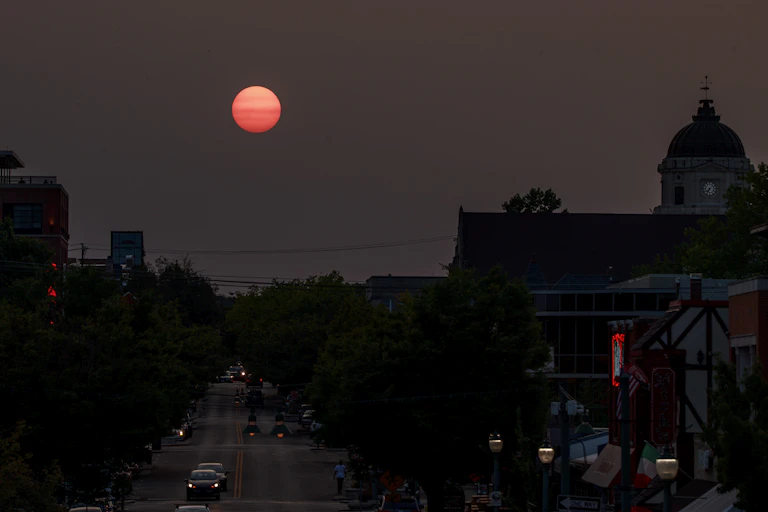A red sun setting over a town with a clocktower.