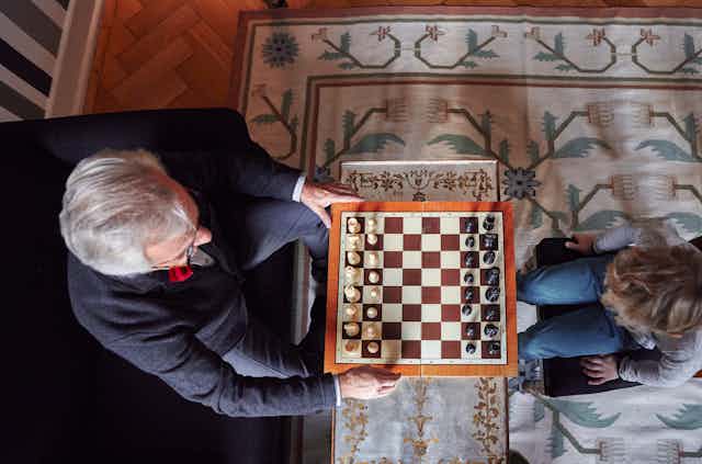 An elderly man plays chess with a child. 