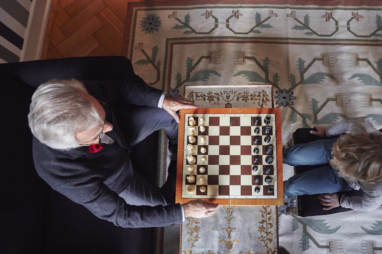 An elderly man plays chess with a child.