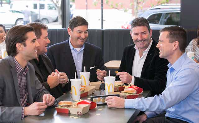 The former CEO of McDonald's is seated at one of the food chain's restaurants while he and others eat Big Macs.