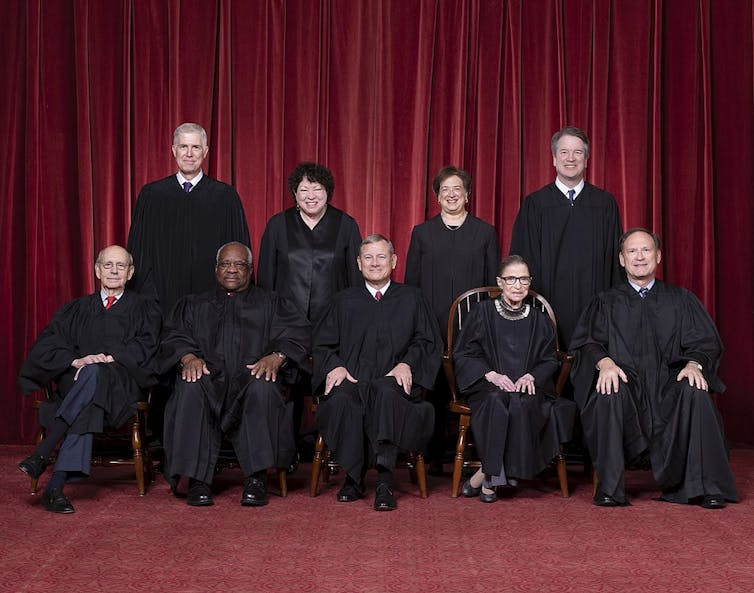 Official portrait of the nine justices wearing their black robes, against a red background