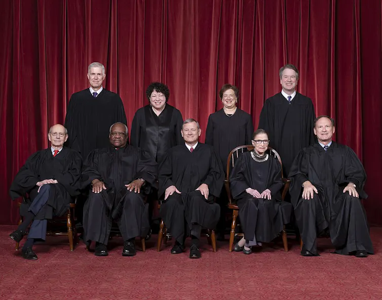 Official portrait of the nine justices wearing their black robes, against a red background