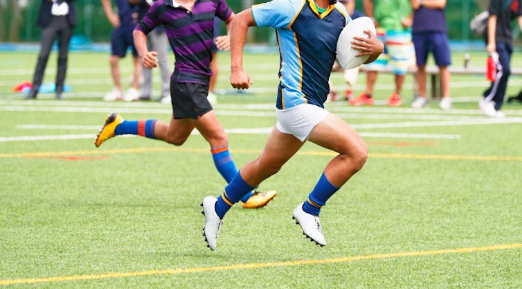 Two players in a game of school rugby, one running with the ball.