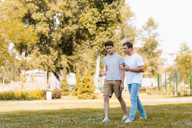 Father and teenage son walking and talking outside in a park.