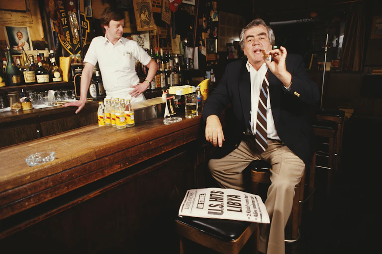 Jimmy Breslin smoking a cigar at a bar.