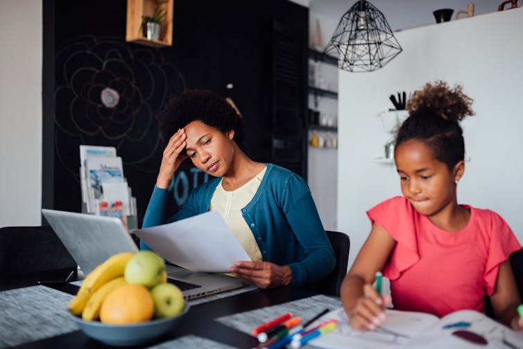 overwhelmed woman at laptop sitting with girl coloring