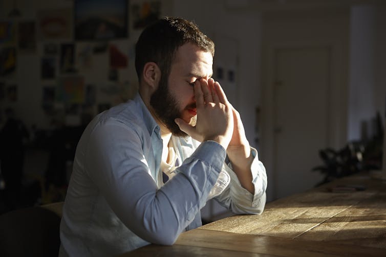 bearded man with eyes closed and hands to his face