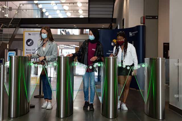 Three women wearing masks swipe their passes at a security gate