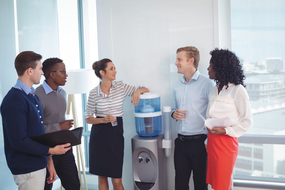 Five people in office clothes stood around a water cooler.