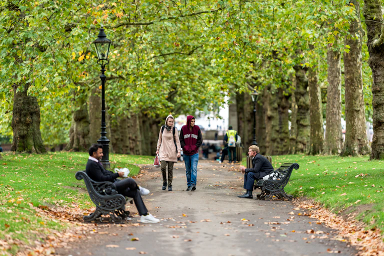 People walking and sitting on benches under trees