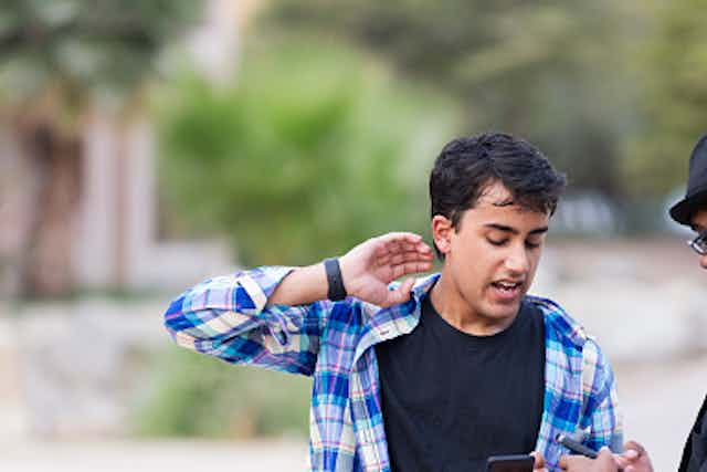 A white student and an African American student engage in an argument outside while holding their phones.