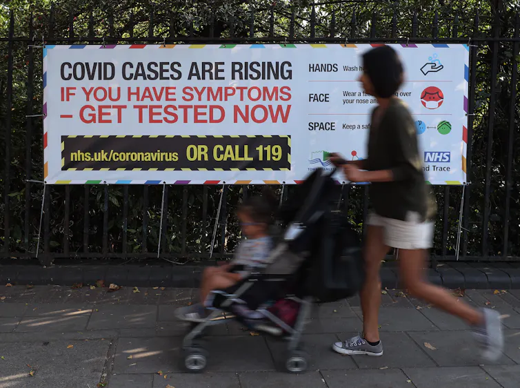 A woman with a pram walks past a sign encouraging people with symptoms of COVID-19 to get tested.