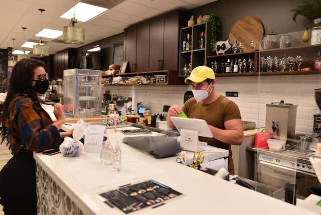 A man and a woman in masks work in an empty restaurant at the counter.