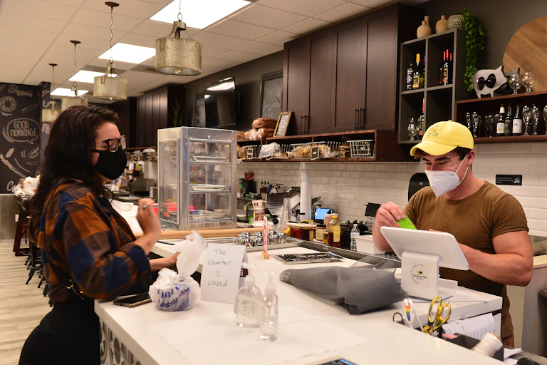 A man and a woman in masks work in an empty restaurant at the counter.