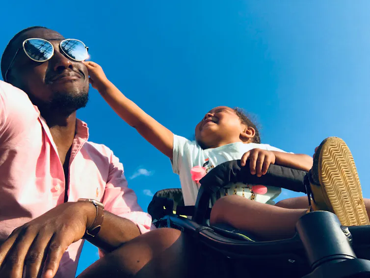 Man with child in pushchair and clear blue sky in background.