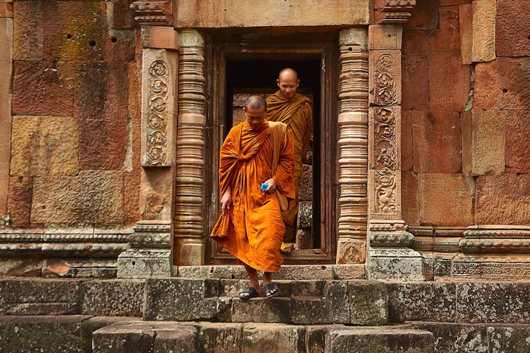 Two monks in orange robes walking down concrete stairs.