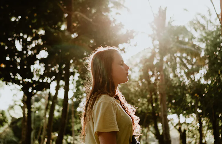 Woman in yellow t-shirt standing in the forest.