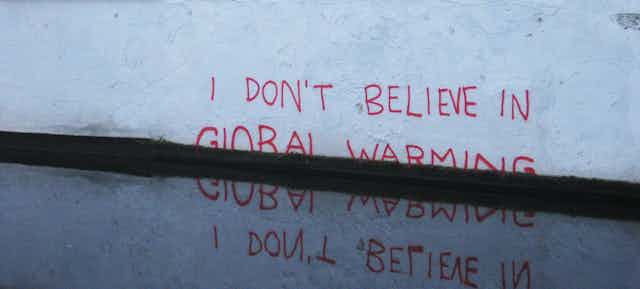 Pintada en una pared blanca que dice No creo en el cambio climático, con varias palabras tapadas por el agua. 