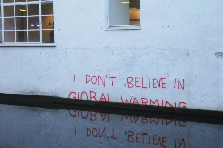 Pintada en una pared blanca que dice No creo en el cambio climático, con varias palabras tapadas por el agua.