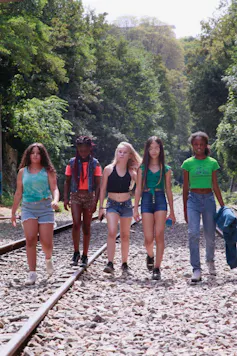 Five girls walk on train track over a gravel road.