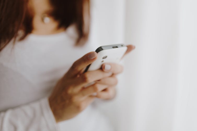 A woman wearing a white long-sleeved shirt holds her phone.