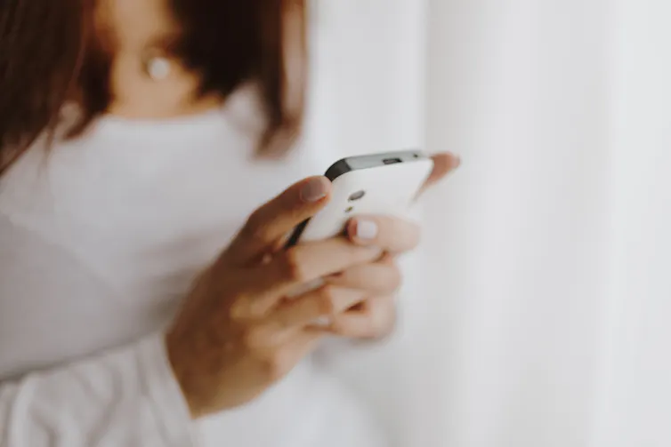 A woman wearing a white long-sleeved shirt holds her phone.