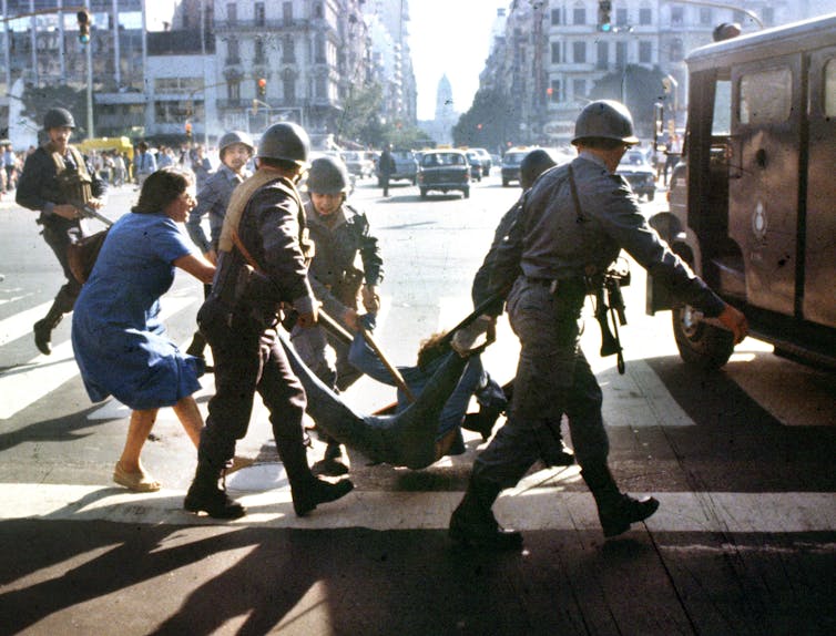 Soldiers drag a person away while another person pulls the other direction.