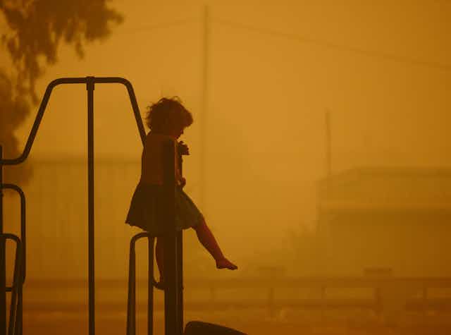 A child sits alone in a playground where the air is yellow due to bushfire smoke.