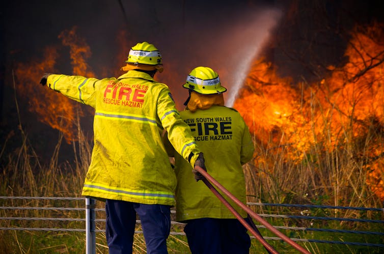 Two firefighters face a blaze.