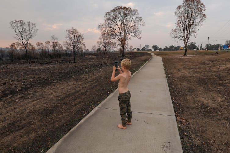 A young child photographs a burnt out landscape