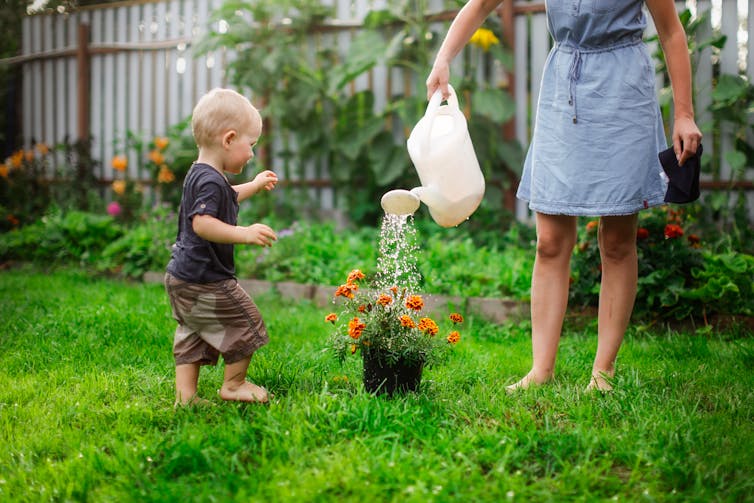 A parent and child water a garden.
