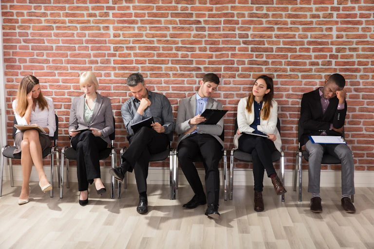 Diverse row of six people sat in front of a brick wall.