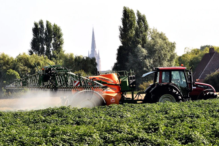 Un tracteur pulvérisant des pesticides sur des cultures.