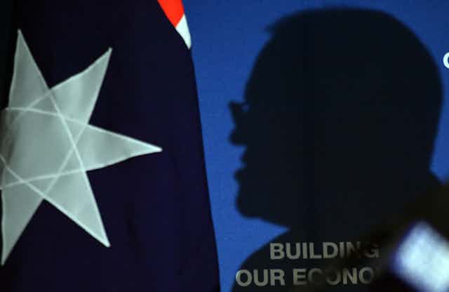 A silhouette of Scott Morrison, cast against an Australia flag