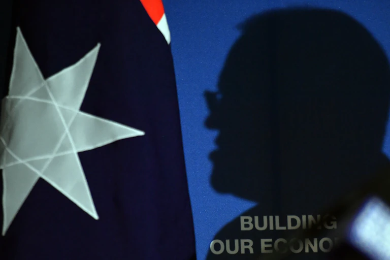 A silhouette of Scott Morrison, cast against an Australia flag