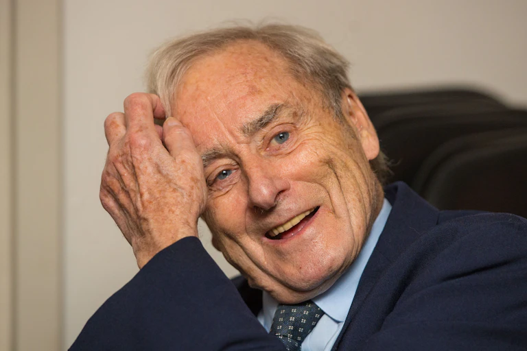 Elderly man smiling and combing his hair with his hand.