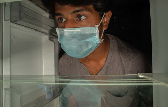 A man wearing a mask opens an empty fridge.