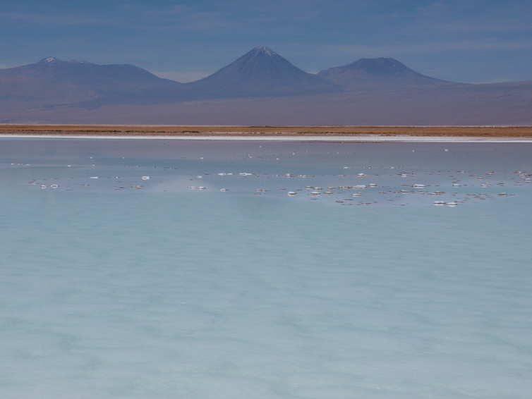 The large lake of Laguna La Brava with active volcanoes behind at sunset.